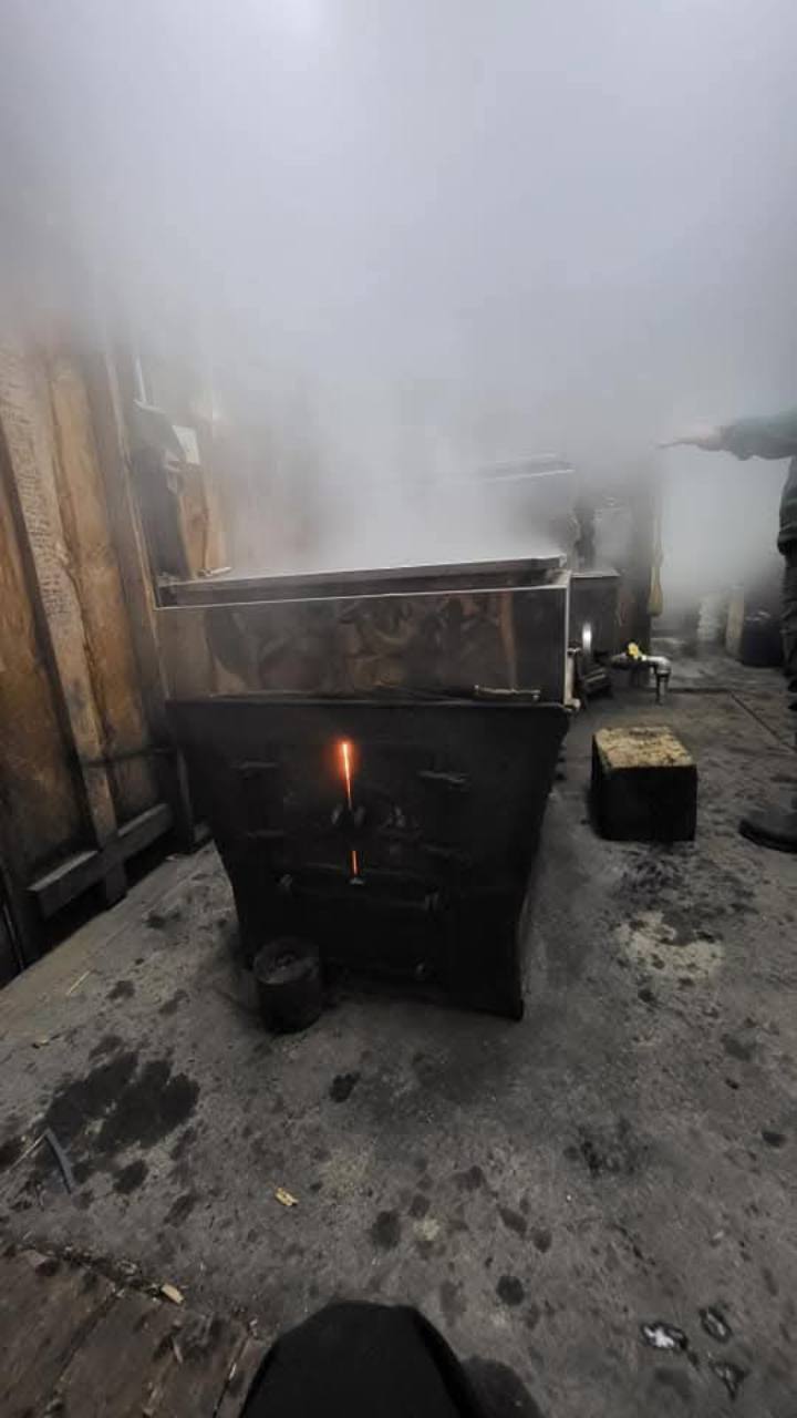 A wood-fired evaporator with a glowing firebox seam and steam rising from the pans