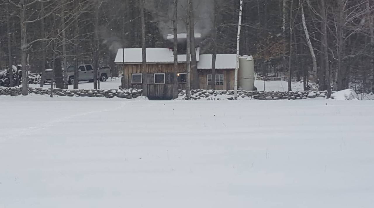 The Knolltop Farm sugarhouse behind a stone wall in the snowy woods